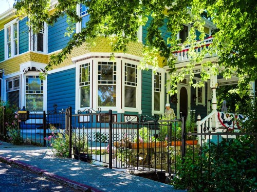 A colorful two-story house with blue siding, surrounded by greenery and a decorative fence.