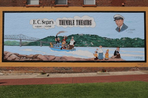 Mural depicting E.C. Segar's "Thimble Theatre," featuring characters on a boat with a scenic background.