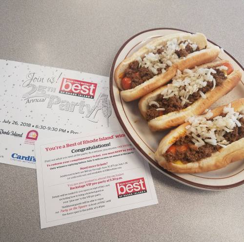 A plate of hot dogs topped with meat, onions, and peppers, alongside an invitation to a party.