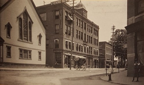 Historic street scene featuring buildings, a church, and horse-drawn carriages in a vintage setting.