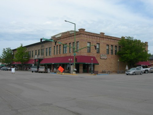 Historic building with red awnings at a street intersection, featuring shops and trees under a cloudy sky.