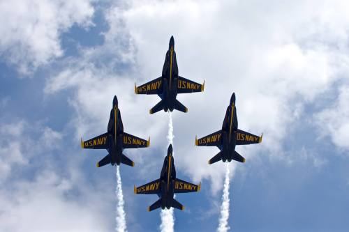Four U.S. Navy jets flying in formation against a cloudy sky, leaving trails of smoke behind them.