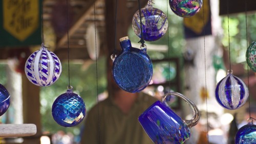 Colorful glass ornaments in various shapes and patterns hanging from strings, with a blurred background.