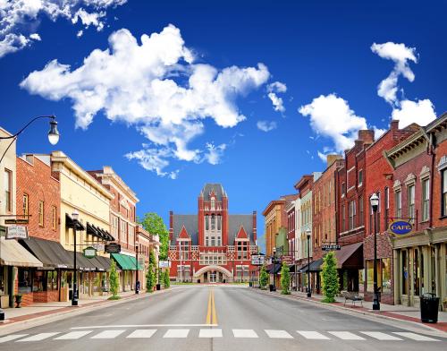 A charming street lined with brick buildings, shops, and a grand architectural structure under a blue sky with clouds.