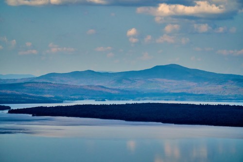 A serene landscape featuring layered mountains and a calm lake under a cloudy sky.