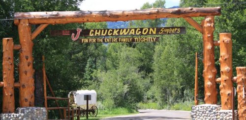 Wooden archway sign for Bar J Chuckwagon Suppers, surrounded by trees, inviting families for nightly fun.