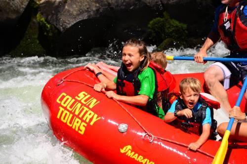 A group of excited children in a red raft navigating whitewater rapids, enjoying a thrilling outdoor adventure.