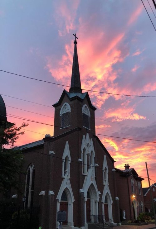 A church with a tall steeple silhouetted against a vibrant sunset sky filled with pink and orange clouds.