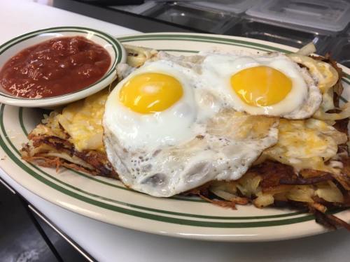 A plate of crispy hash browns topped with two sunny-side-up eggs, served with a side of salsa.