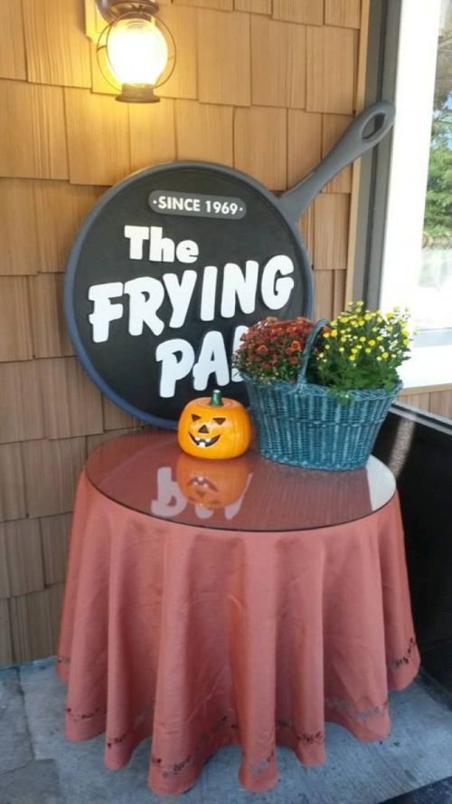 A table with an orange tablecloth, a jack-o'-lantern, and a basket of flowers beside a sign for "The Frying Pan."