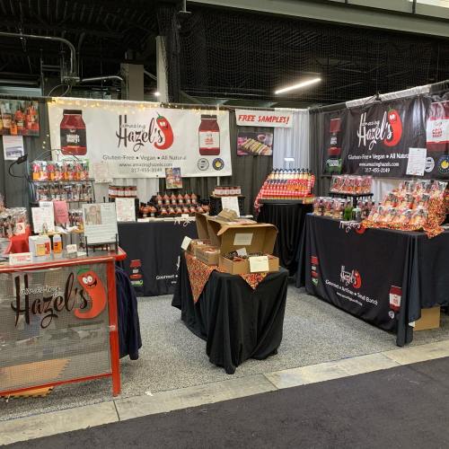 A vibrant vendor booth showcasing gluten-free, vegan products with colorful displays and a sign offering free samples.