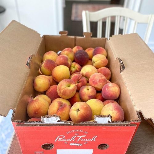 A cardboard box filled with fresh, ripe peaches, sitting on a table.