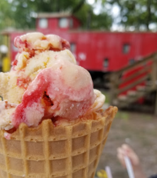 A close-up of a colorful ice cream cone with a red train car in the background.