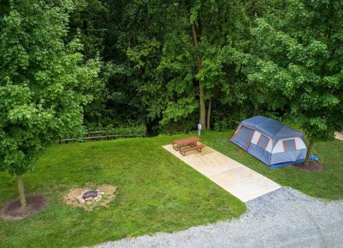 A campsite with a tent, picnic table, and fire pit surrounded by lush green trees.