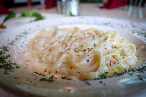 A plate of creamy fettuccine alfredo garnished with herbs, served in a white dish.