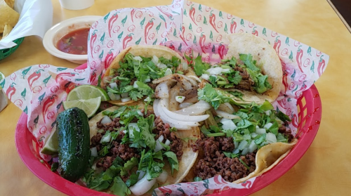 A vibrant basket of tacos filled with meat, onions, and cilantro, accompanied by lime and a jalapeño pepper.