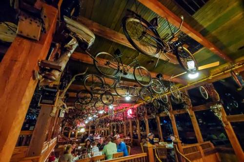 A rustic restaurant interior with bicycles hanging from the ceiling and diners enjoying their meals below.
