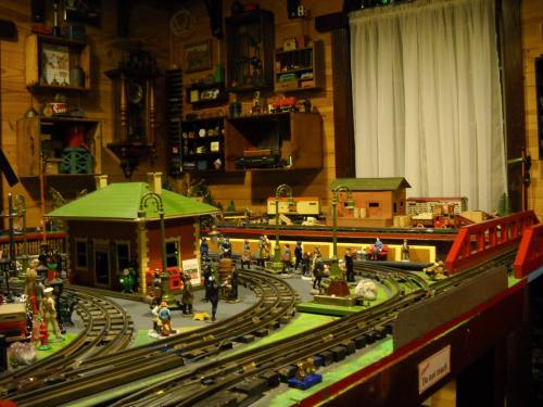 A detailed model train setup with tracks, buildings, and miniature figures in a cozy room.