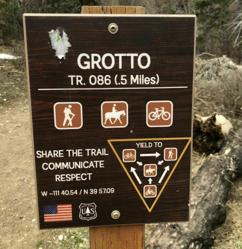 Trail sign for Grotto (TR. 086, 0.5 miles) with icons for hikers, horses, and cyclists, emphasizing trail sharing and respect.