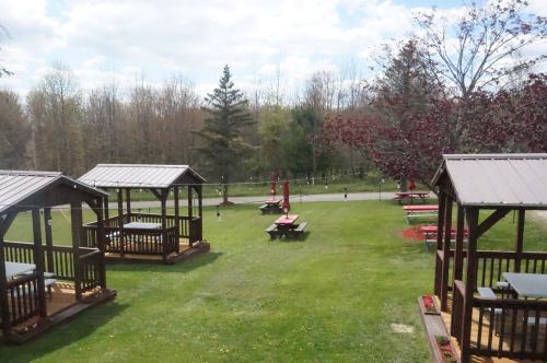 A scenic outdoor area with wooden gazebos, picnic tables, and lush greenery under a partly cloudy sky.