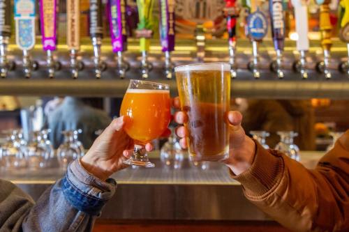 Two people clink glasses of beer at a bar, with a variety of beer taps in the background.