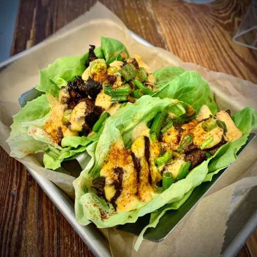 Two lettuce wraps filled with grilled chicken, green onions, and spices, served on a metal tray.