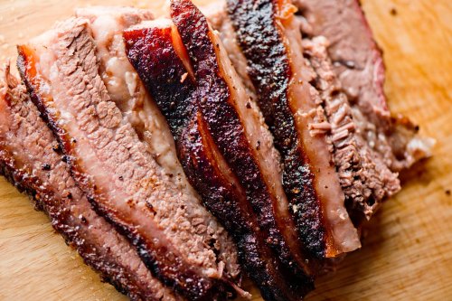 Sliced brisket on a wooden cutting board, showcasing a smoky crust and tender meat.