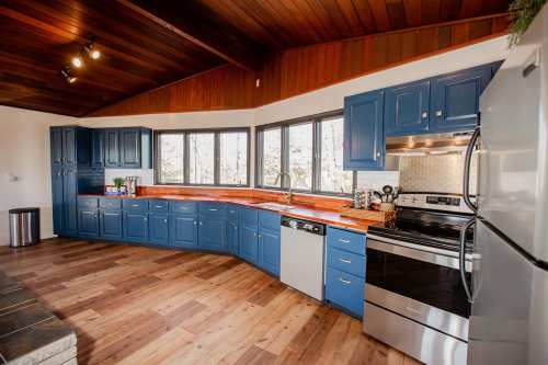 Modern kitchen with blue cabinets, stainless steel appliances, and a wooden ceiling, featuring a spacious countertop and windows.