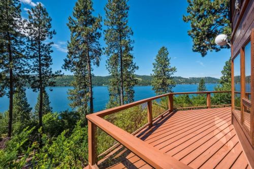 Scenic view from a wooden deck overlooking a tranquil lake surrounded by tall pine trees under a clear blue sky.