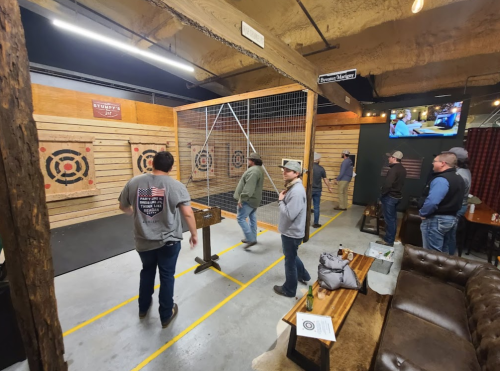 Axe-throwing venue with several people practicing, targets on wooden walls, and a cozy seating area in the background.