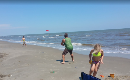 A man throws a frisbee while a girl plays nearby on a sandy beach with gentle waves in the background.