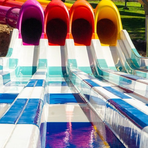 Colorful water slides in a sunny park, featuring vibrant red, orange, and yellow tubes against a blue and white surface.