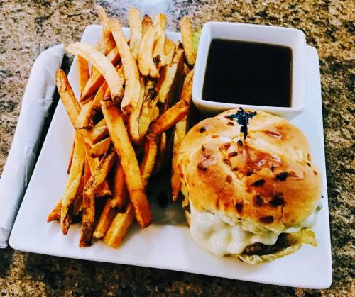 A plate with a cheeseburger on a bun, served with crispy fries and a small bowl of dipping sauce.