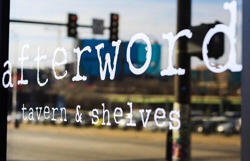 Sign reflecting the cityscape, reading "afterword tavern & shelves" on a glass window.