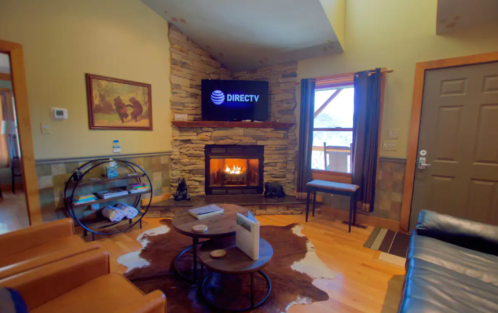 Cozy living room with a stone fireplace, TV, leather chairs, and a coffee table on a cowhide rug.