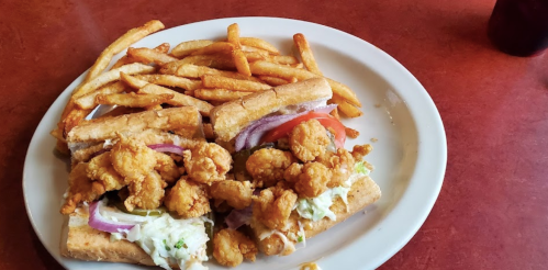 A plate with a sandwich filled with fried shrimp, lettuce, and tomato, accompanied by a side of golden fries.