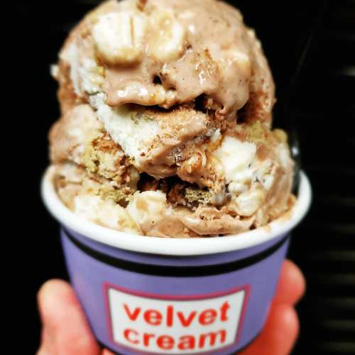A hand holding a cup of chocolate and vanilla ice cream with cake pieces, labeled "velvet cream."