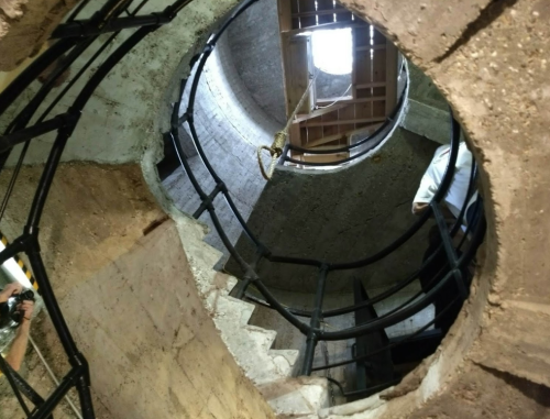 A spiral staircase inside a cylindrical structure, with a light source visible at the top.