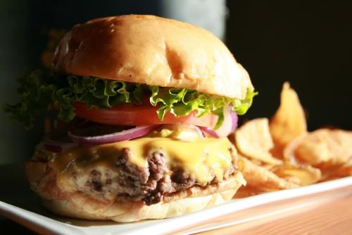 A juicy cheeseburger with lettuce, tomato, and onion, served with a side of potato chips on a white plate.