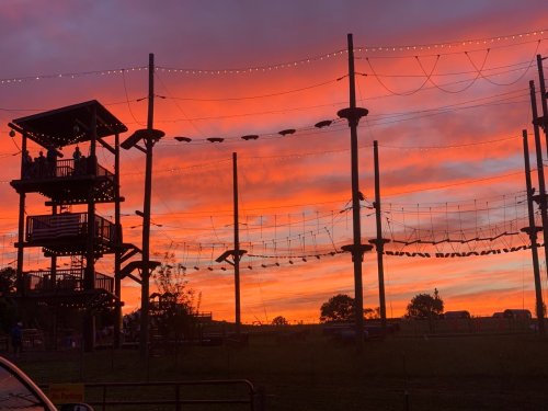 Silhouette of a climbing structure against a vibrant sunset with orange and pink hues.