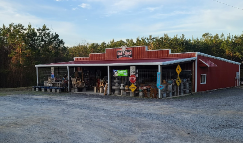 A red barn-style store with outdoor furniture and signs, surrounded by trees and gravel.