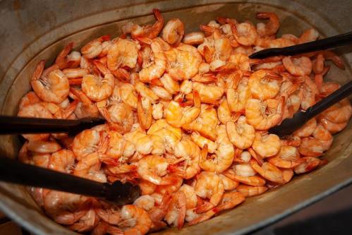 A large metal tray filled with cooked shrimp, with tongs resting on top for serving.