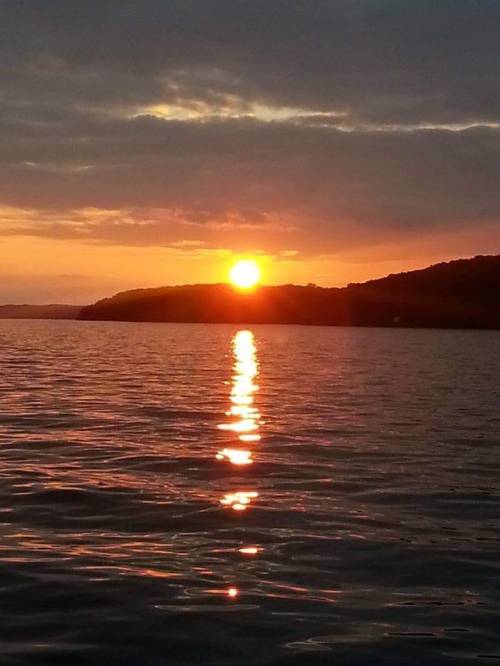 A serene sunset over calm waters, with vibrant orange and yellow hues reflecting on the surface.