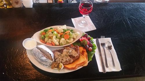 A plate with a grilled steak, baked potato, mixed vegetables, and a glass of red drink on a black table.