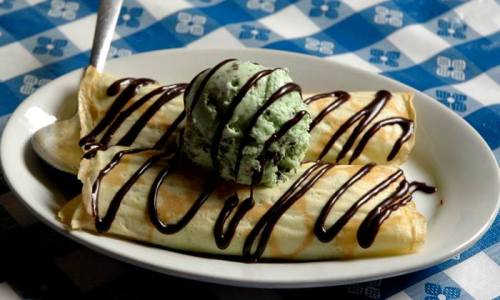 Two crepes drizzled with chocolate sauce, topped with a scoop of mint ice cream, served on a white plate.