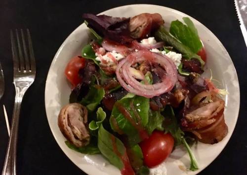 A colorful salad with mixed greens, cherry tomatoes, red onions, and pieces of meat, drizzled with dressing.