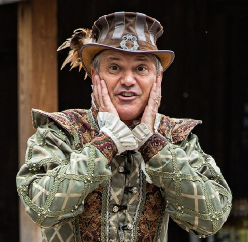 A man in a decorative costume and hat, expressing surprise with his hands on his cheeks.