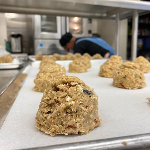 Close-up of cookie dough mounds on parchment paper, with a person preparing food in the background.