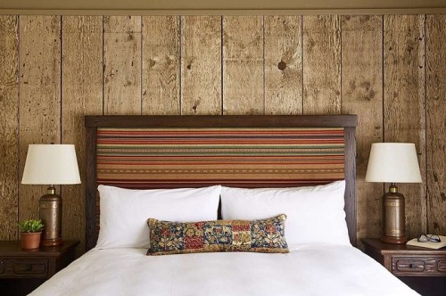 Cozy bedroom with a wooden accent wall, a striped headboard, two lamps, and a decorative pillow on a white bed.
