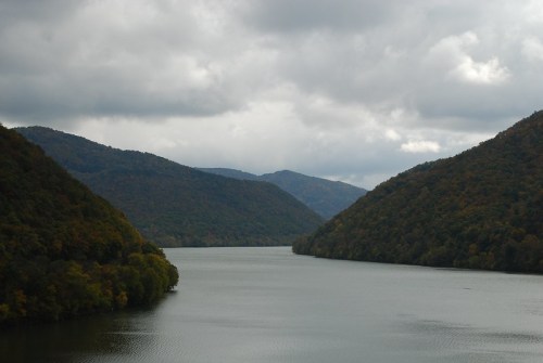 A serene river flows between lush, green mountains under a cloudy sky.